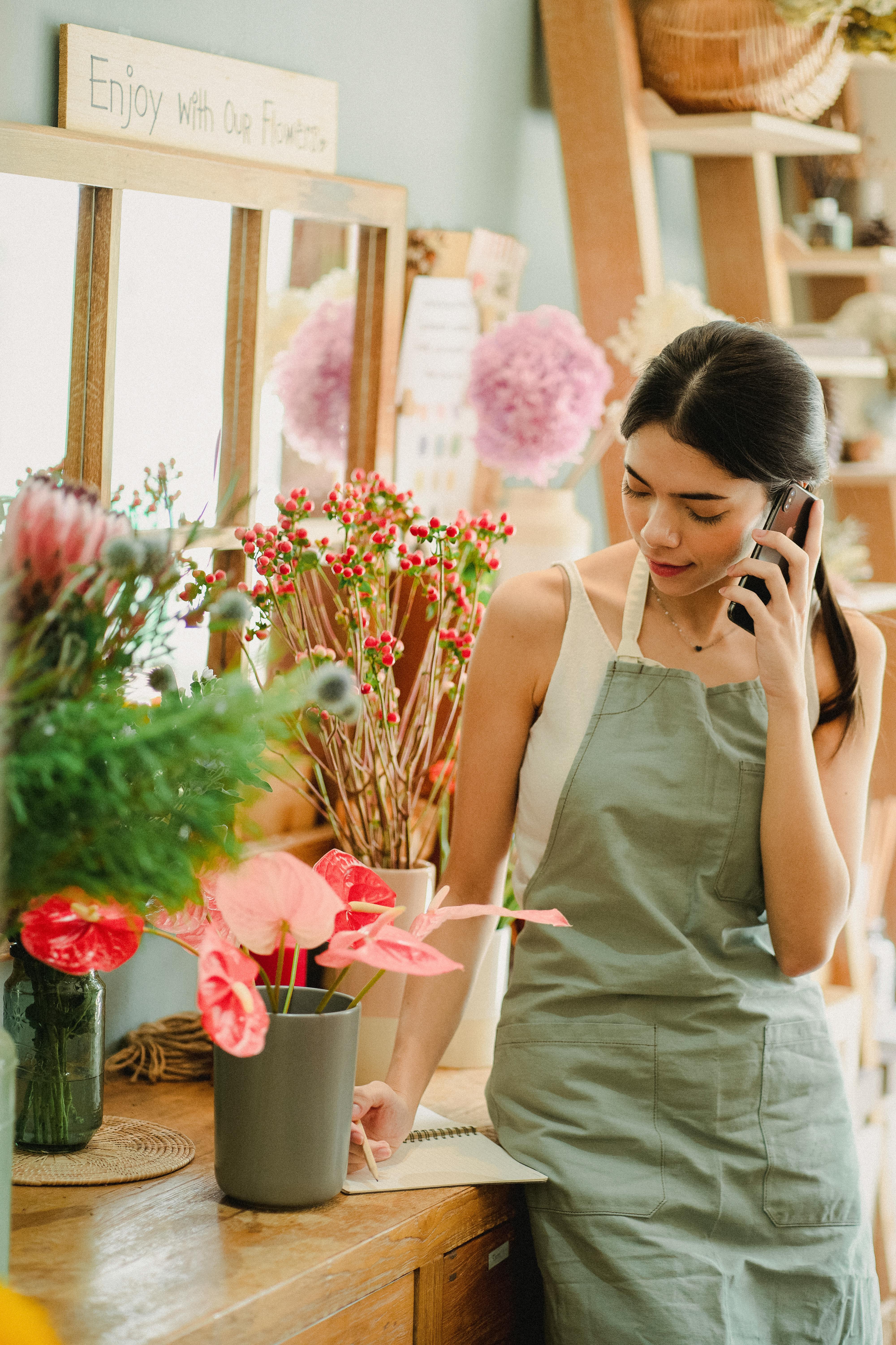 female florist talking on phone and writing notes in shop