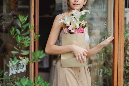 一位女士拎着装有美丽花束的纸袋走出了花店