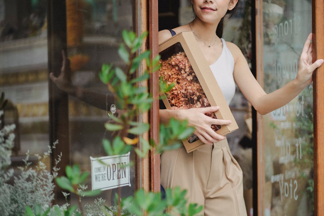 Crop glad woman with dried flowers box leaving floristry store