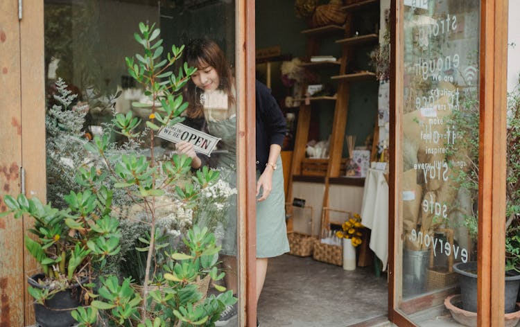 Asian Florist Turning Signboard On Store Wall