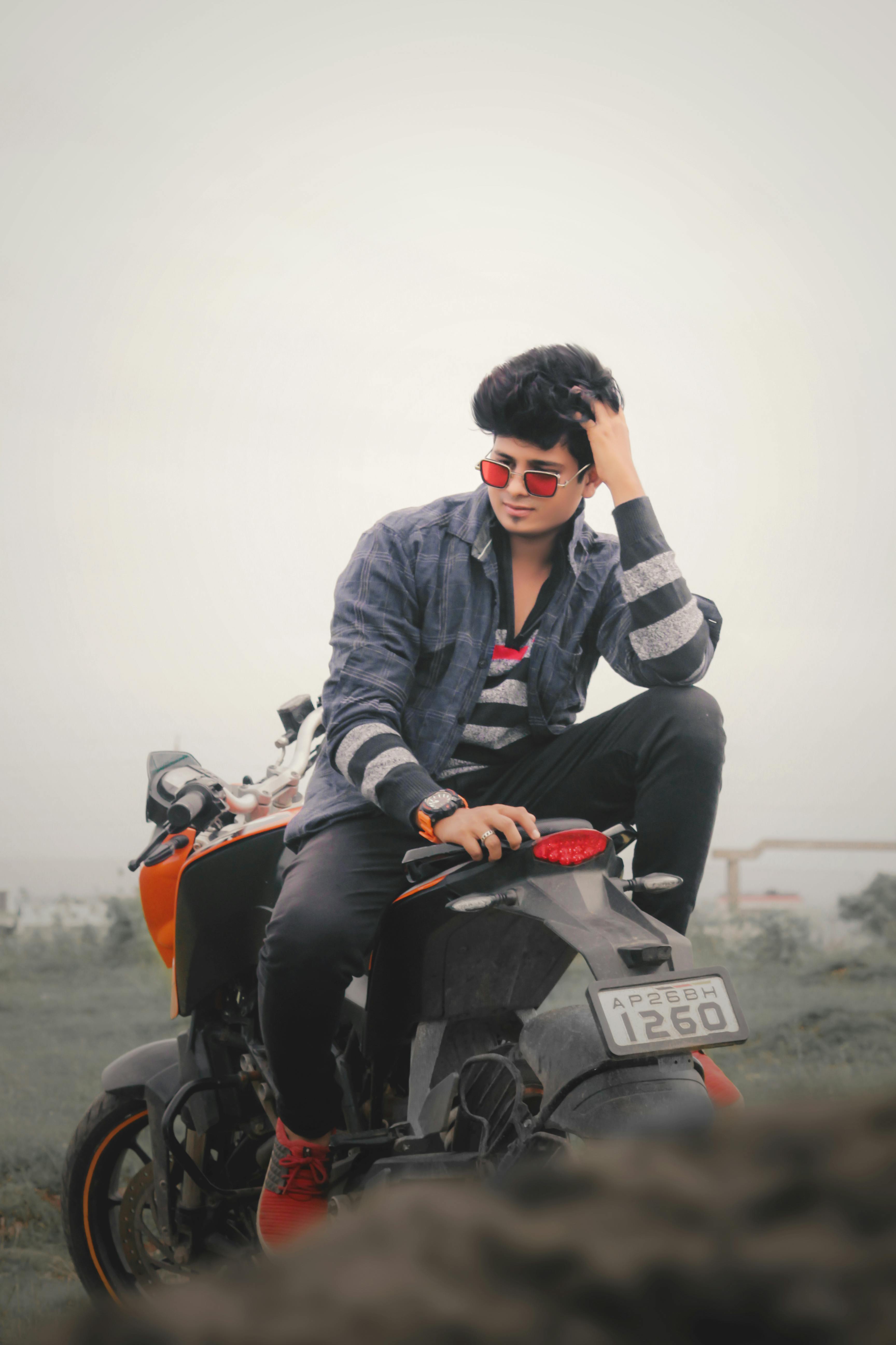 Young man in sunglasses poses confidently on a motorcycle in an open field.