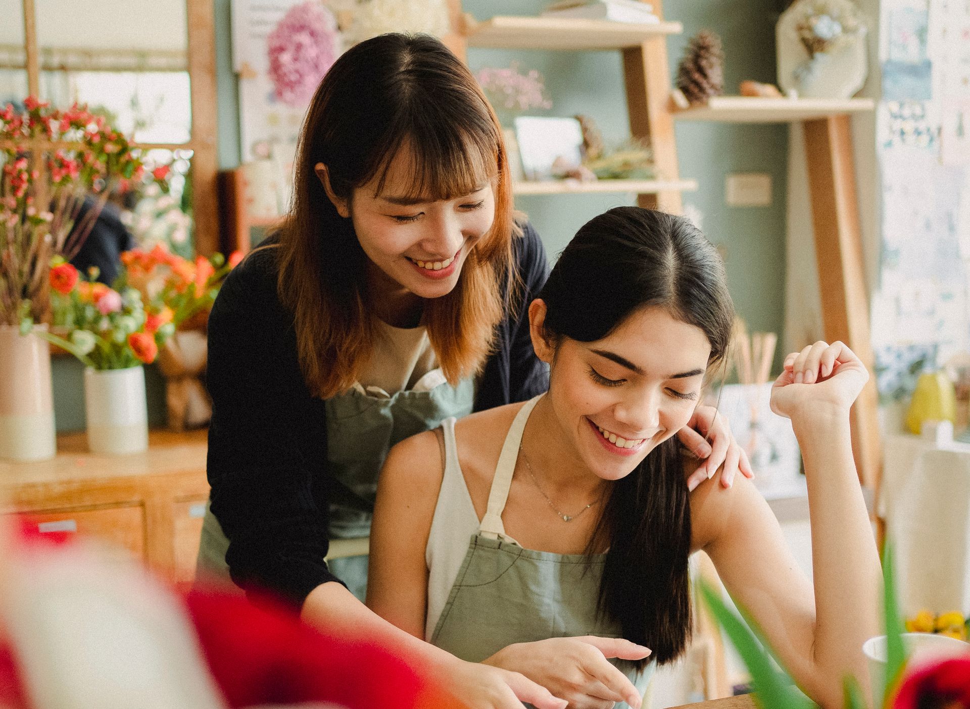 Cheerful multiracial women in casual clothes and aprons creating arrangement in floristry studio during workshop in daytime