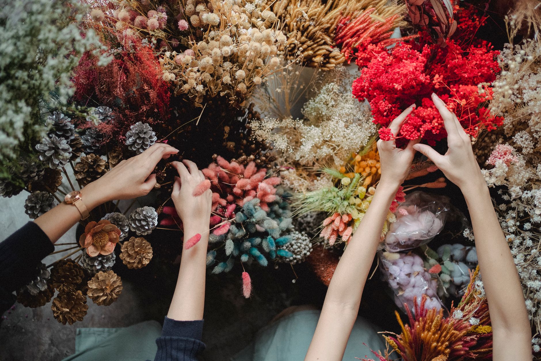 Top view of crop unrecognizable women standing near table and choosing dried flowers during workshop in daytime