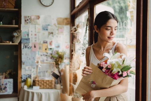 一位安静的女子穿着休闲服，白天离开室内舒适的花店，手里拎着装满鲜花的纸袋