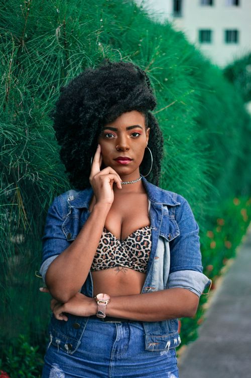 Free Stylish woman poses outdoors in denim and leopard print outfit, blending bold fashion and natural greenery. Stock Photo