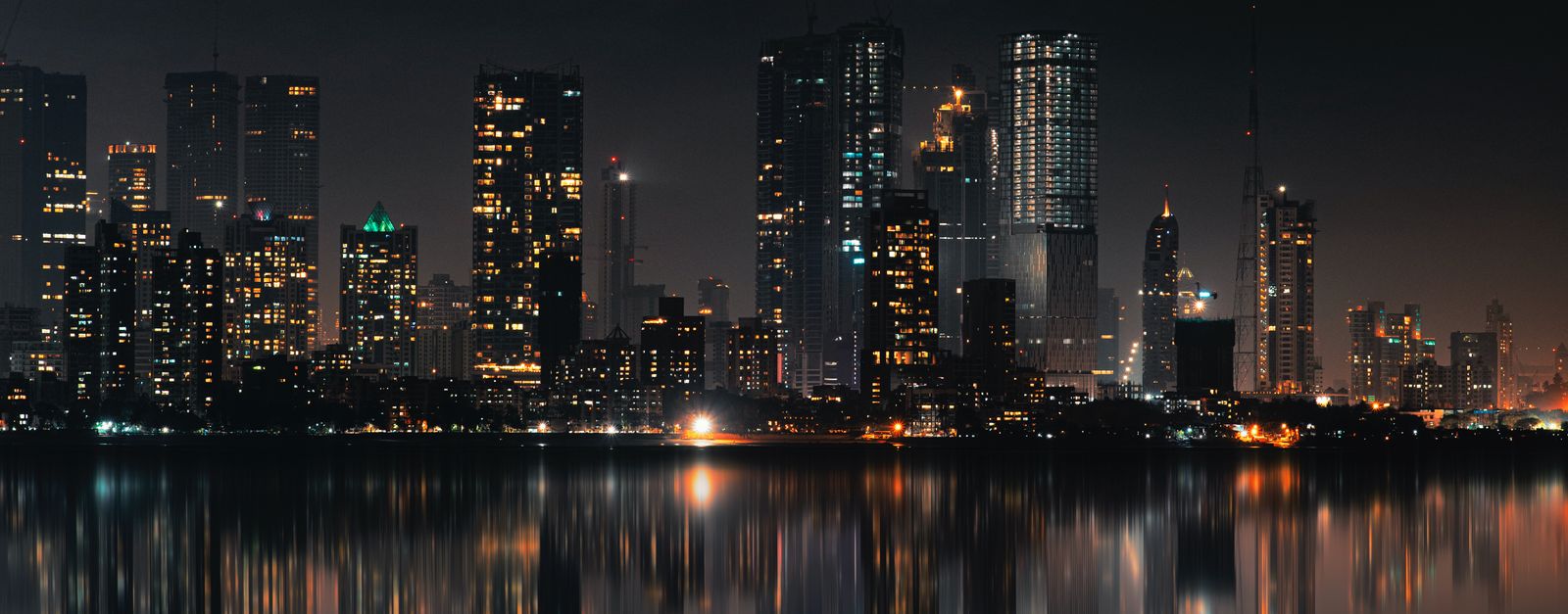 Captivating night view of Mumbai skyline with skyscrapers and reflections on still water.