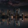 The brightly illuminated modern skyline of Mumbai reflects across the still water at night.