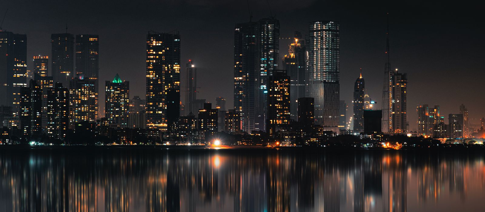 Captivating night view of Mumbai skyline with skyscrapers and reflections on still water.