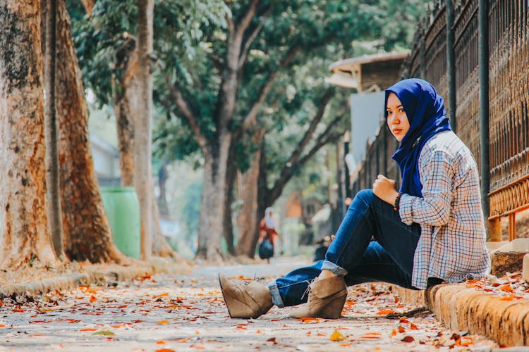 Young Woman In Hijab Sitting On A Pavement Curb In City In Autumn 