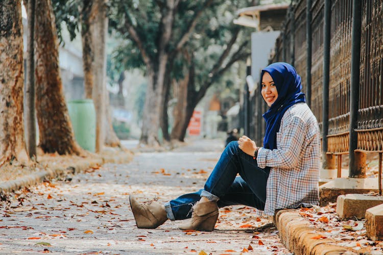 Young Woman In Hijab Sitting On A Pavement Curb In City In Autumn 