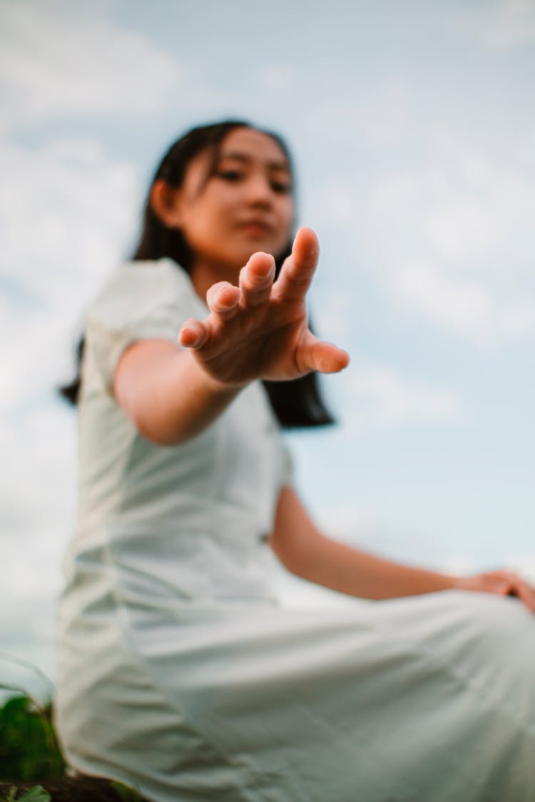 Asian Teen In White Dress Reaching Arm Under Cloudy Sky