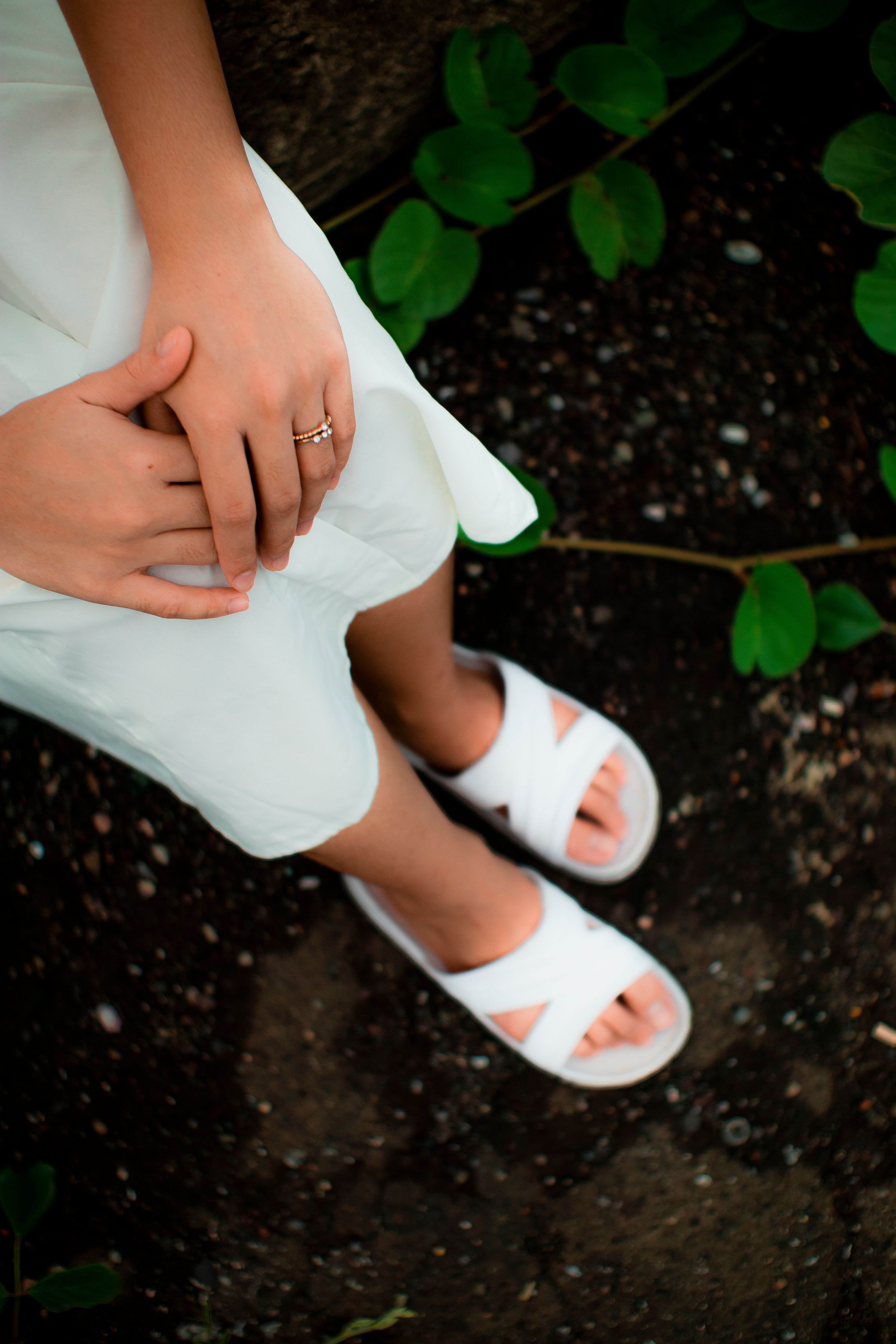 From above of crop anonymous female in trendy dress and white sandals standing on terrain near plant in garden