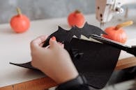 一只手的特写镜头切开了黑色毛毡蝙蝠万圣节工艺品，背景是南瓜