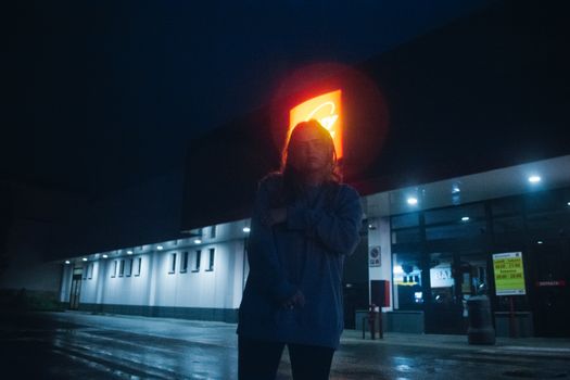 夜晚，一名女子站在灯火通明的建筑外，身旁的霓虹灯招牌亮着光，营造出一种忧郁的城市氛围