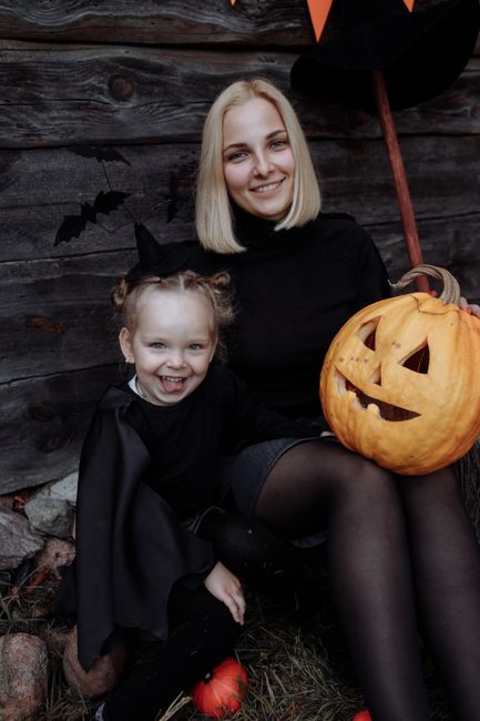 A joyful mother and daughter in costumes celebrate Halloween with a carved pumpkin.