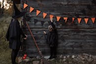 万圣节期间，一对身着女巫服装的母女在木墙上挂起了三角旗横幅