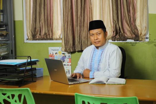 Successful Indonesian teacher working at a desk in a traditional outfit.