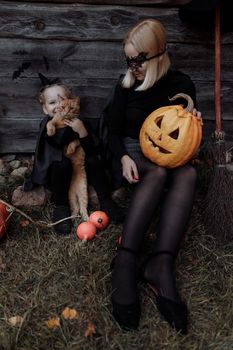妈妈和女儿穿着女巫服装，在户外与南瓜和猫一起庆祝万圣节