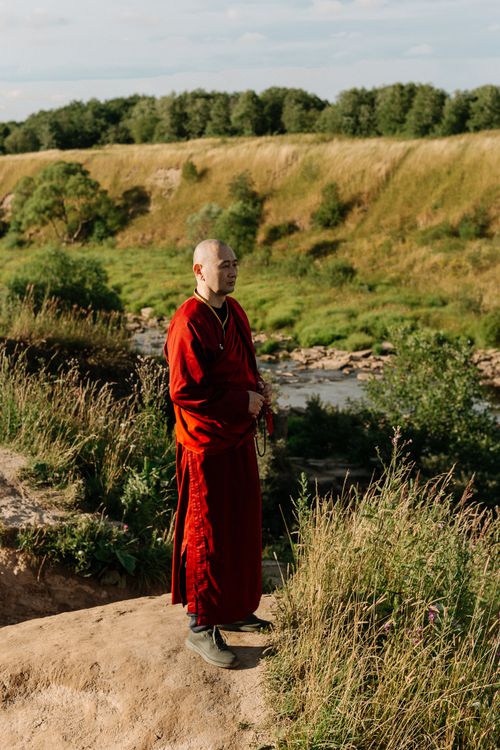 Free A Buddhist monk in a red robe stands in a tranquil outdoor setting by a river. Stock Photo