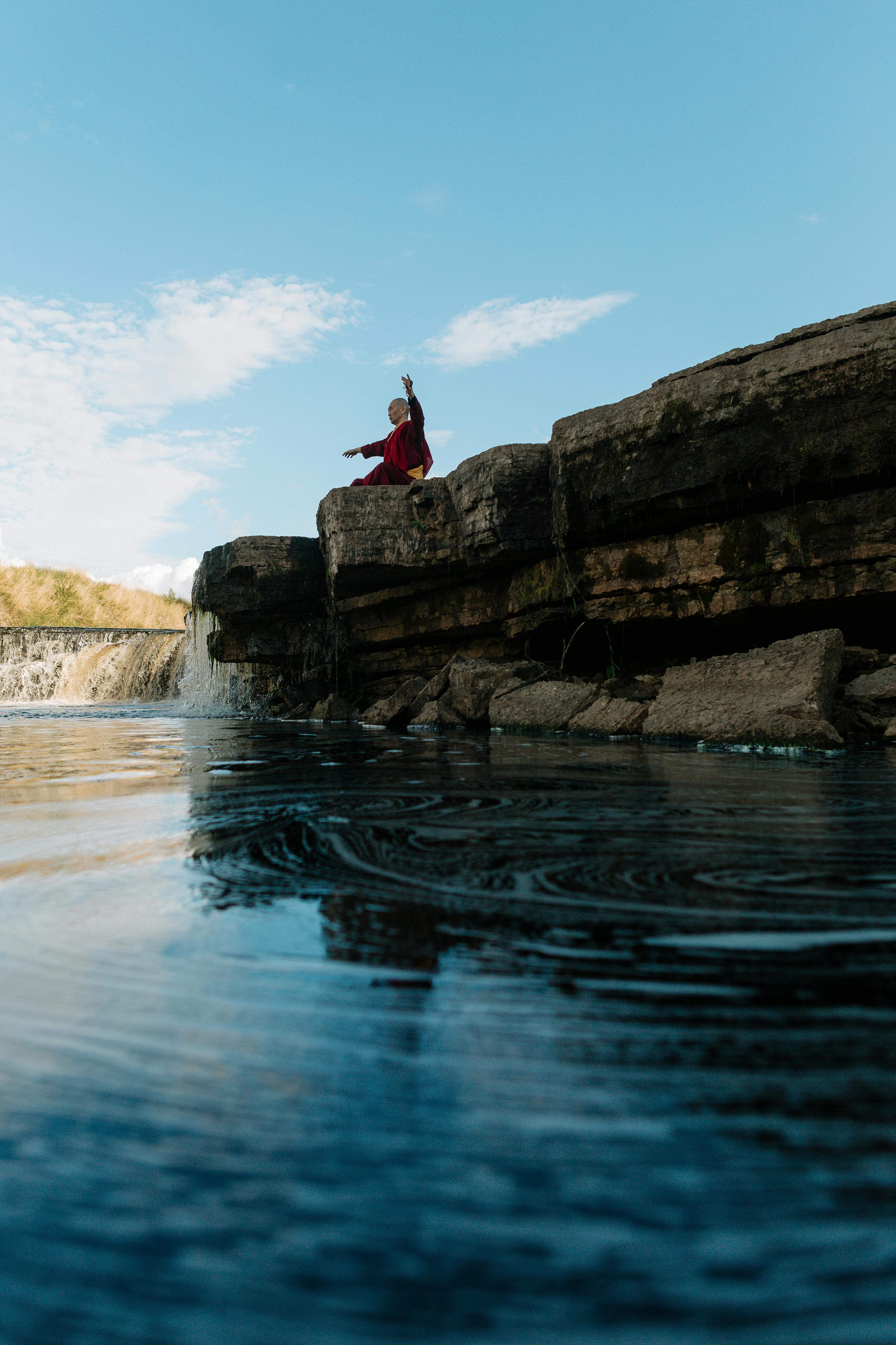 一位僧人坐在岩石悬崖上冥想，俯瞰晴朗天空下宁静的河流