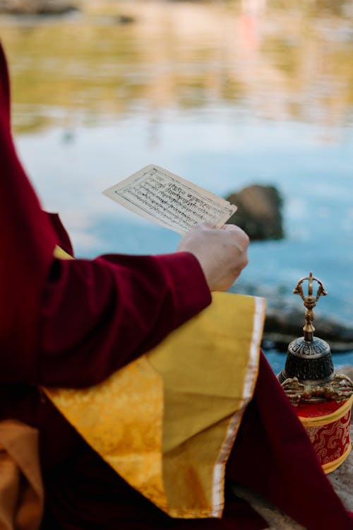 Buddhist Monk Reading a Prayer from a Piece of Paper while Sitting by the River