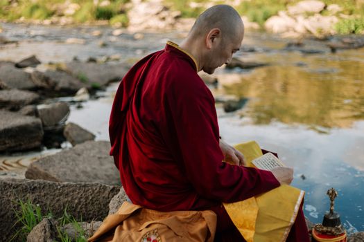 A Buddhist monk in deep meditation by a tranquil riverside setting during autumn.