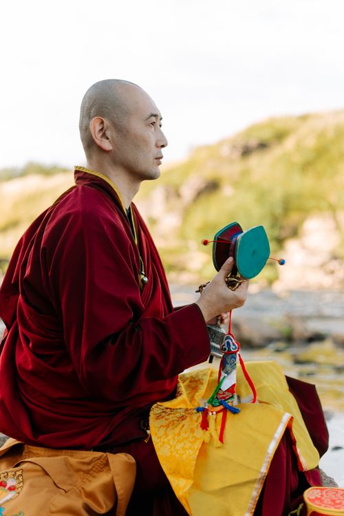 Free A Buddhist monk in traditional robes sits in meditation with a Tibetan prayer wheel outdoors. Stock Photo