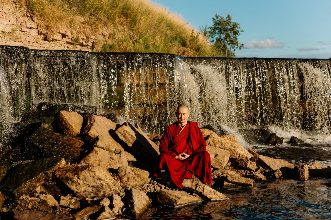 Woman in Red Robe Sitting on Rock Near Waterfalls