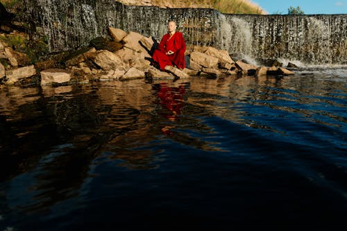川の岩の上に座っている赤いジャケットの男