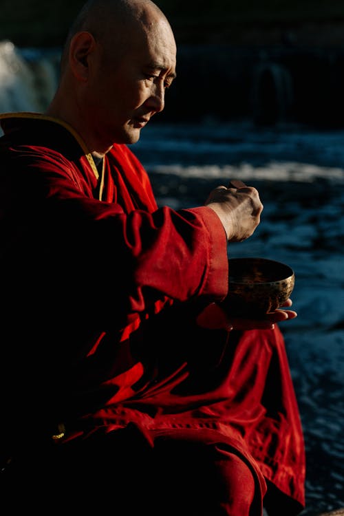 Man in Red Robe Holding a Brass Bowl