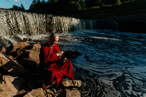 женщина в красно черном платье сидит на скале у реки