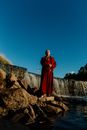 蔚蓝的天空下，一位僧人在瀑布旁冥想，构成一幅宁静的场景