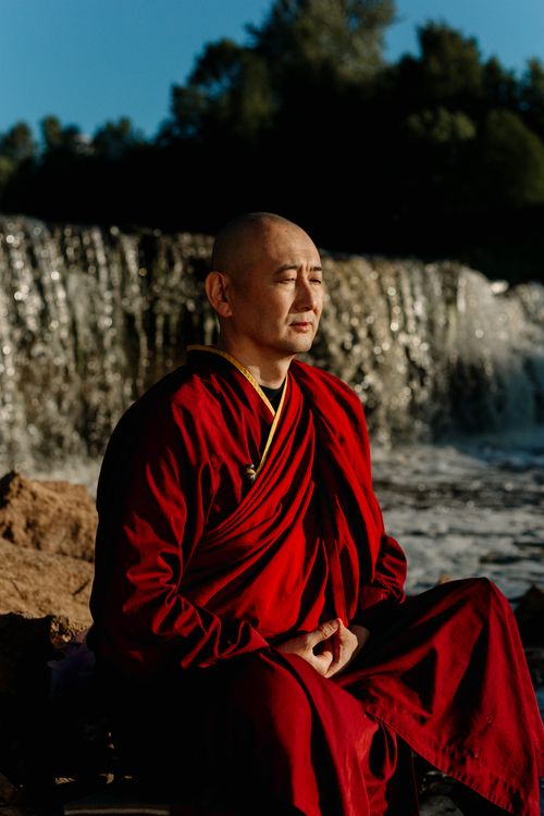 Free A Buddhist monk in red robes sits peacefully meditating by a serene waterfall. Stock Photo