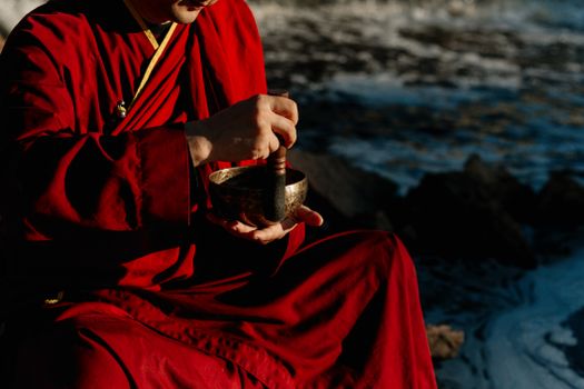 一位身穿红衣的僧人在海边用西藏歌碗演奏，以促进和平与健康