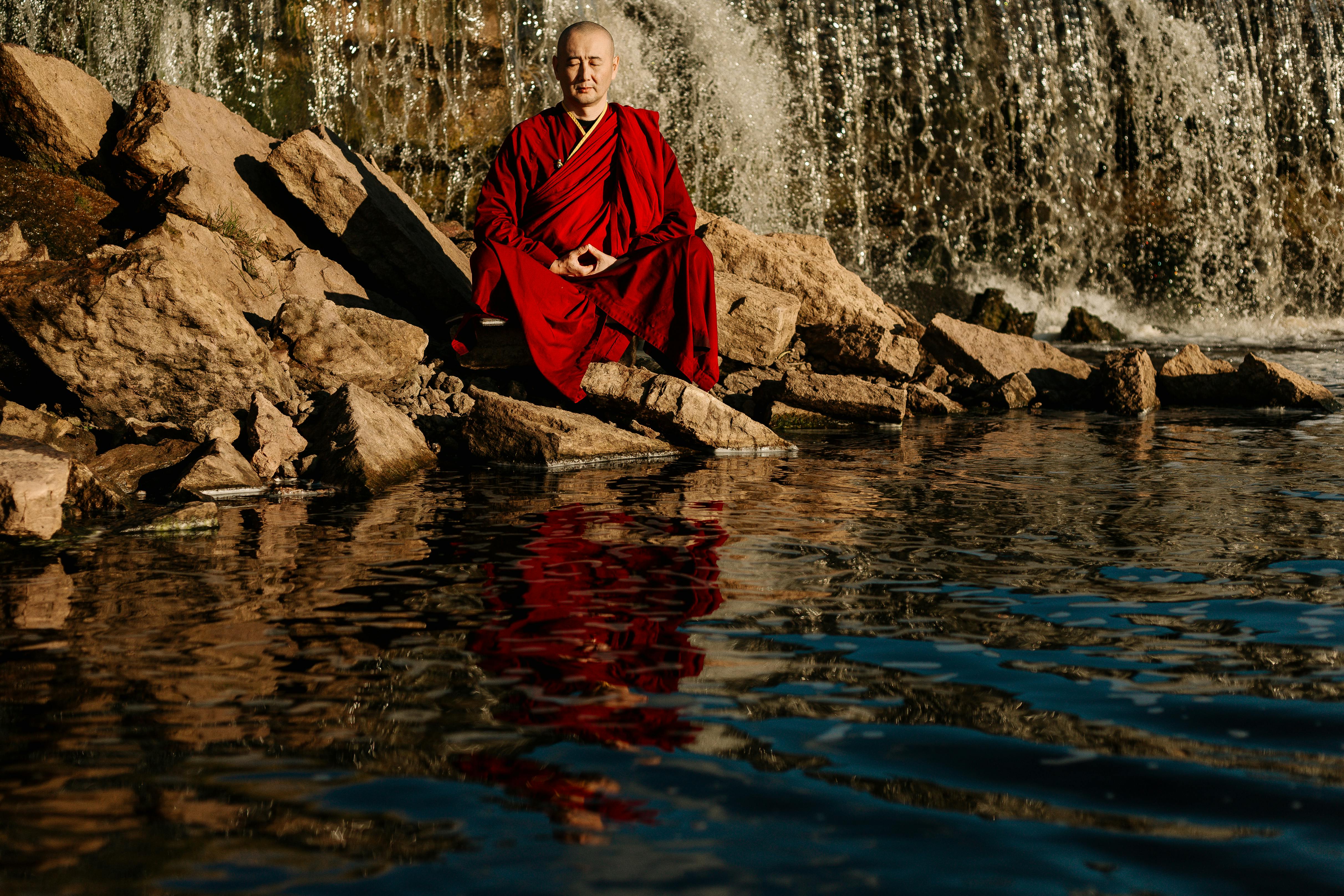 woman in red dress sitting on rock in water