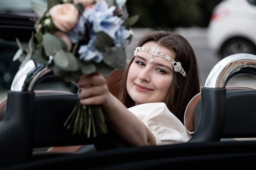 Happy bride with bouquet sitting in cabriolet