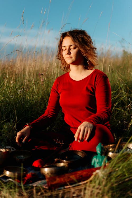 A Woman in Red Long Sleeve Dress Meditating on Grass Field
