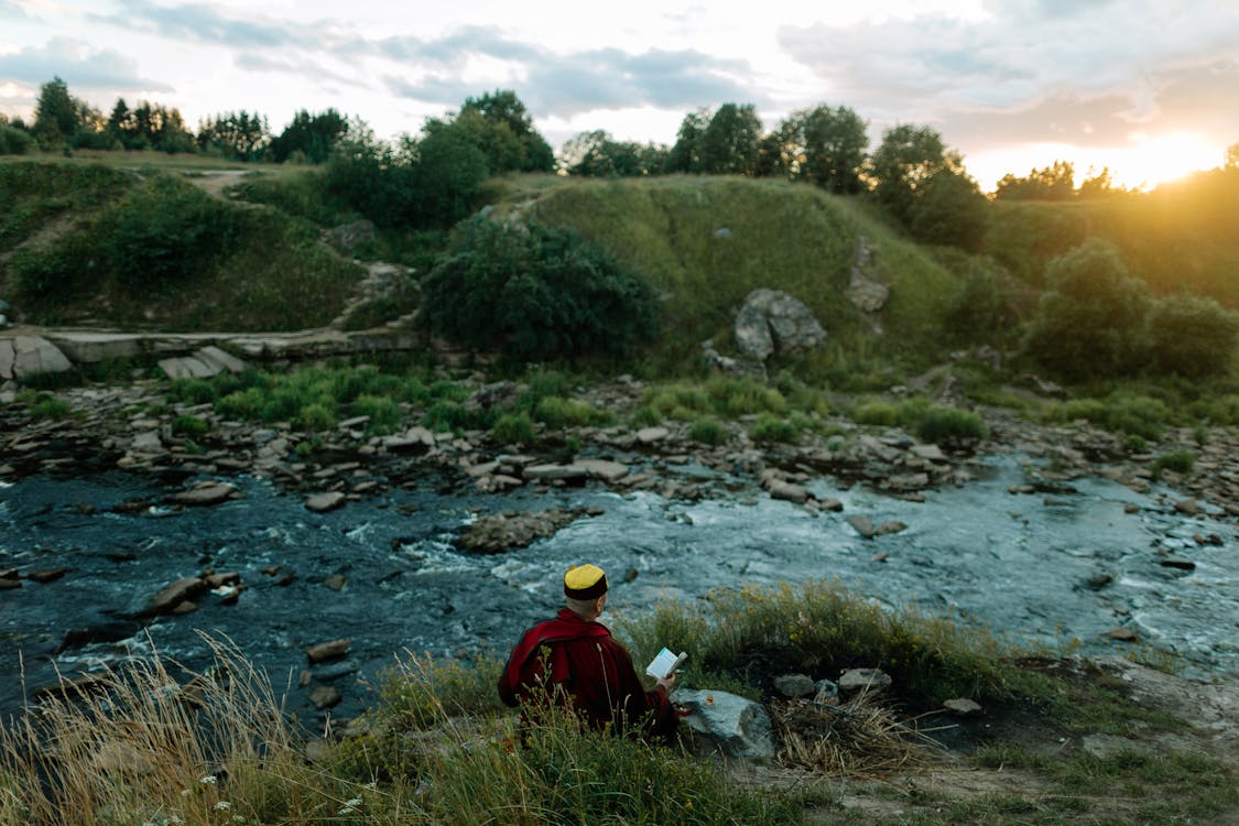 Tibetan Monk Reading a Book Sitting on the Riverbank