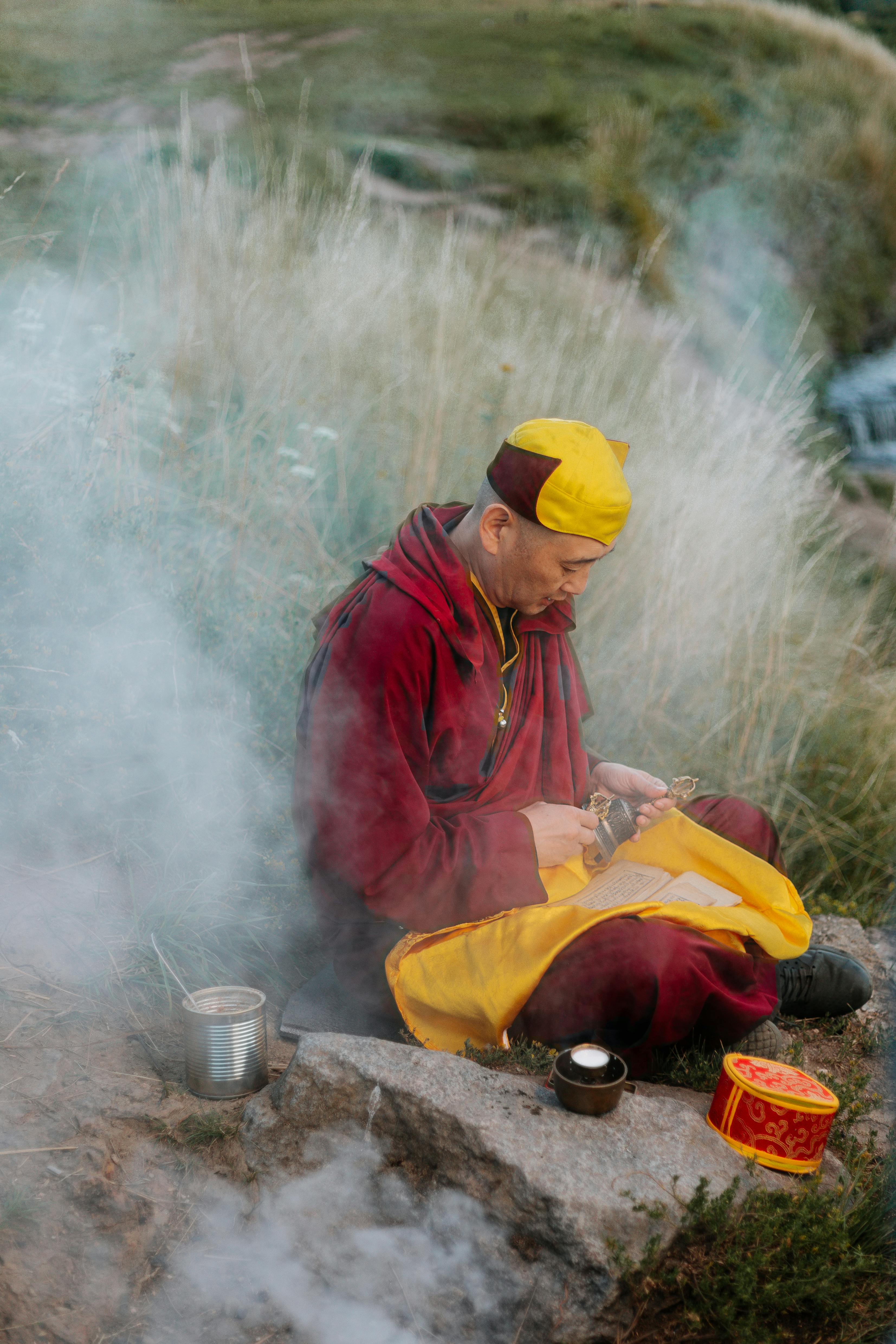 僧人平静地在户外冥想，四周环绕着大自然和仪式物品