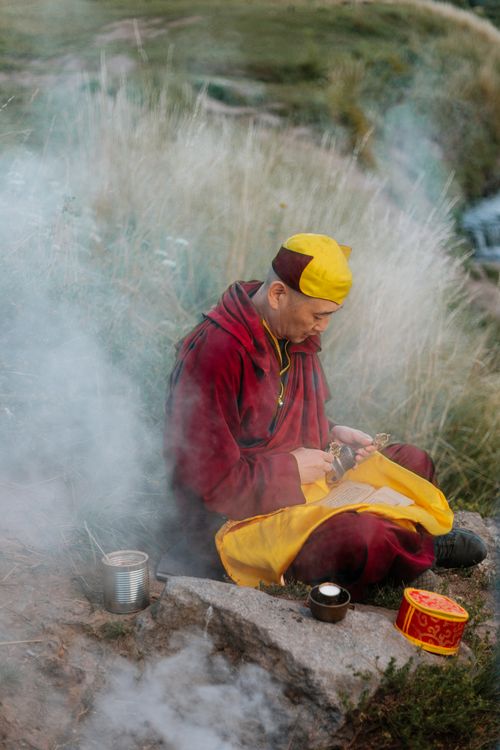 Free Buddhist monk meditating peacefully outdoors surrounded by nature and ritual objects. Stock Photo