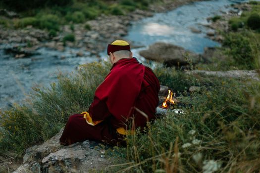 一位僧人在河边冥想，附近燃着一小堆篝火，场景宁静
