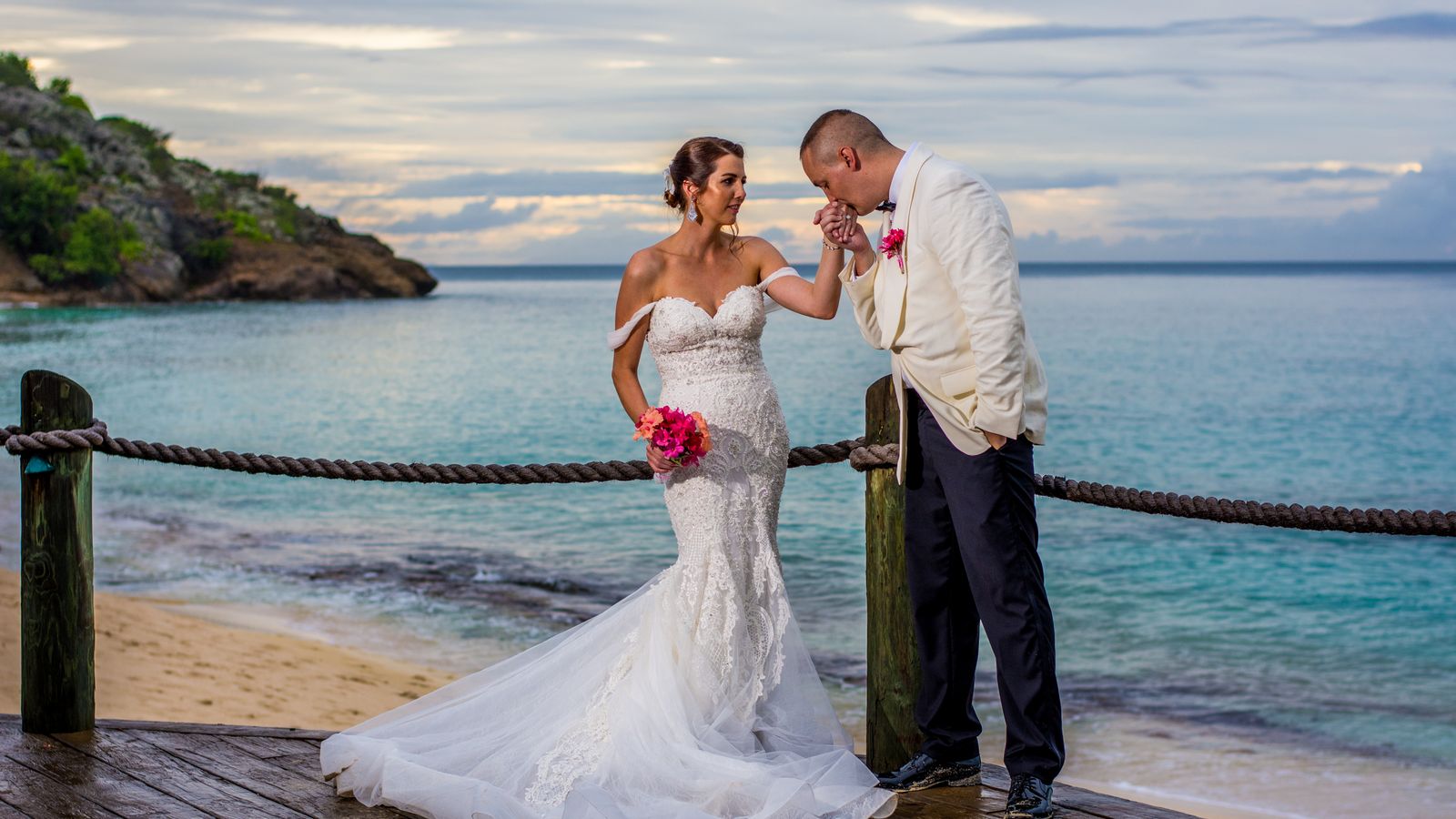Newlyweds share a romantic moment on a beachfront deck in Antigua, captured during sunset with the ocean as a backdrop.