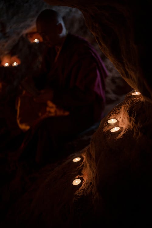 Buddhist Monk Praying in a Cave Lit up by Candles