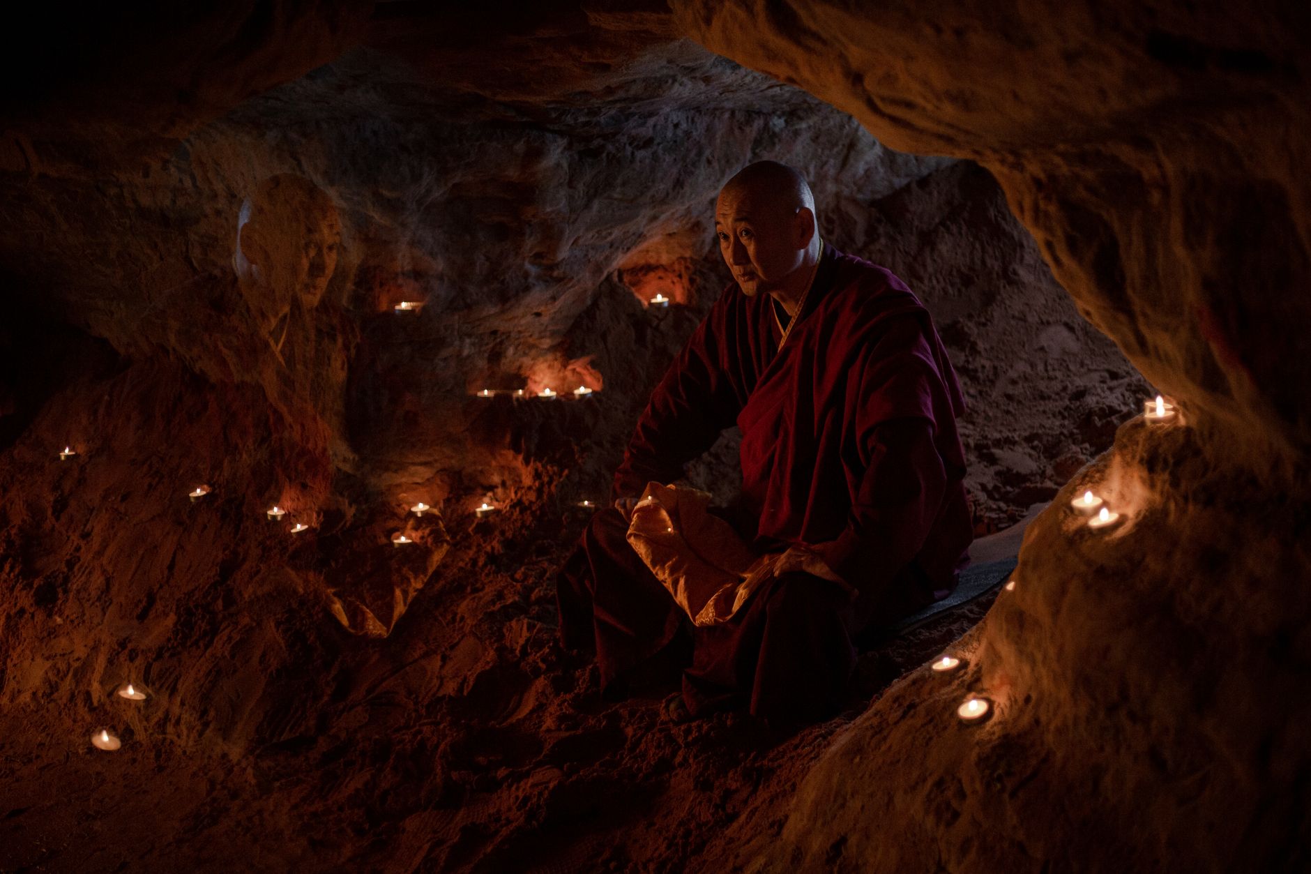 A monk meditates in a candlelit grotto, creating a serene and spiritual atmosphere.