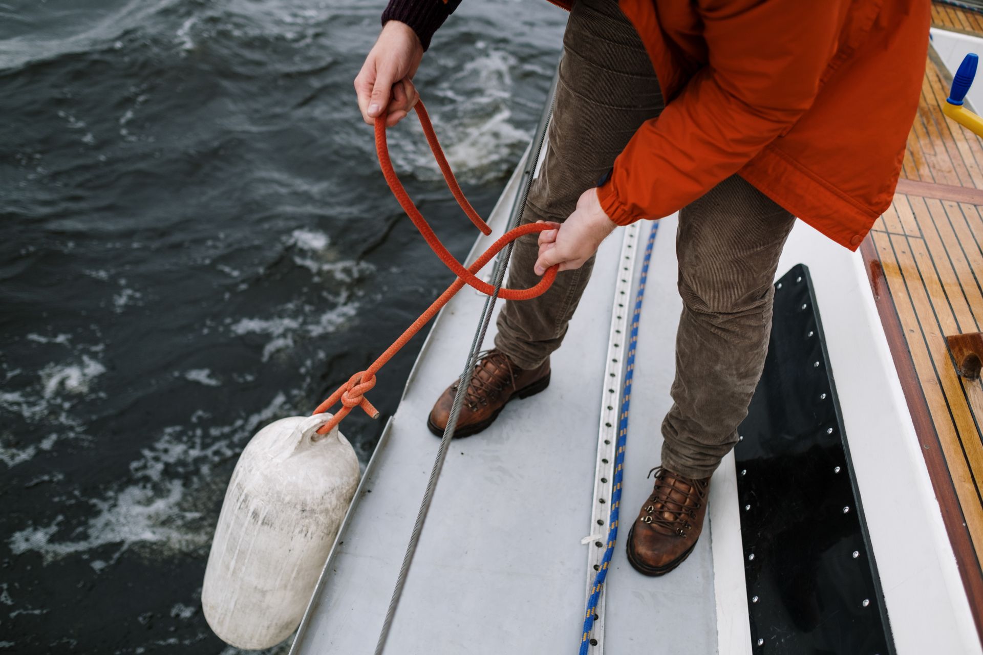 A person tying a rope to secure a buoy on a boat, showcasing boating skills and safety.