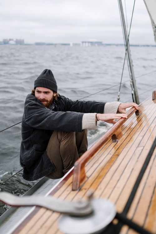 Free Man in beanie holding wooden railing on a boat sailing in choppy waters. Stock Photo