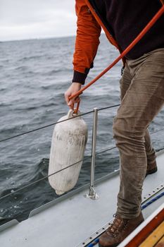 在波涛汹涌的海况中，一个人正在调整帆船栏杆上的浮标，展示航海活动