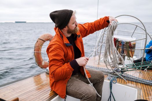 Man sitting on a yacht, managing ropes during a nautical journey at sea.