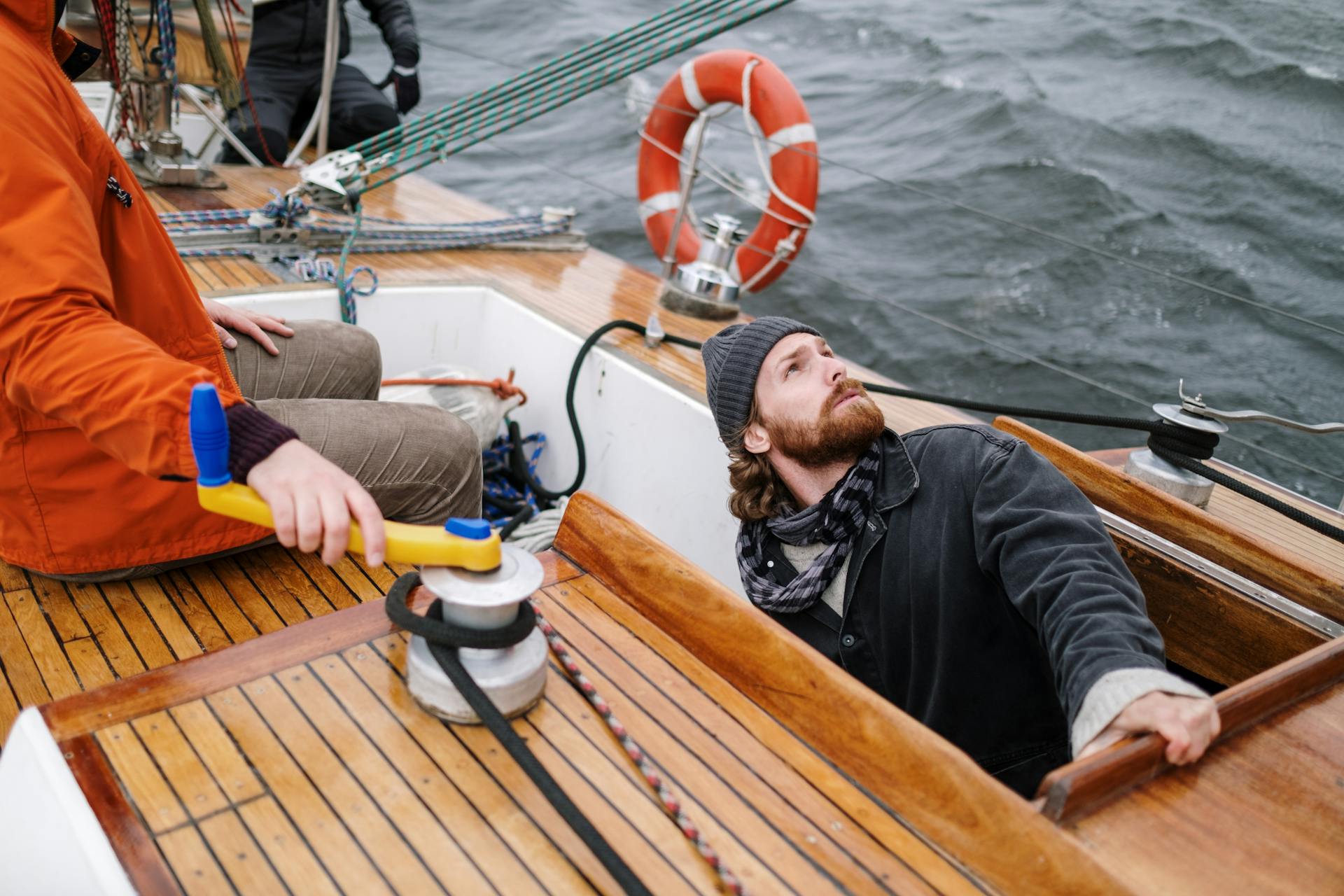 Two sailors navigating a wooden yacht on open waters, showcasing teamwork and adventure.