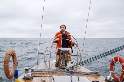 Free A man confidently steering a sailboat in the vast ocean under a cloudy sky, exploring adventure. Stock Photo